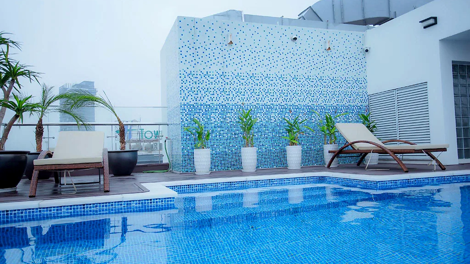 Hồ bơi rooftop khách sạn 4 sao phong cách hiện đại với ghế thư giãn và mảng mosaic xanh.