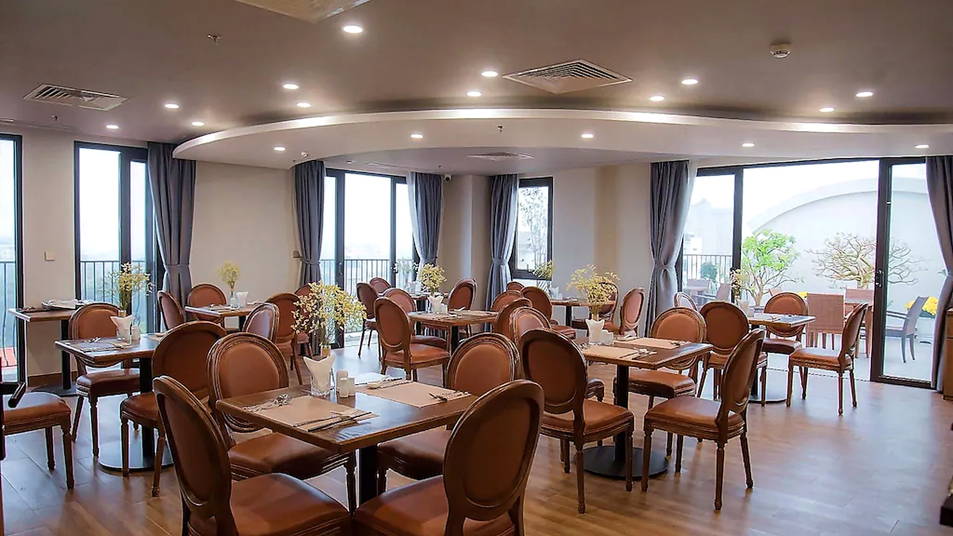 Nhà hàng khách sạn 4 sao có không gian rộng, bàn ghế gỗ và hệ cửa kính lớn.