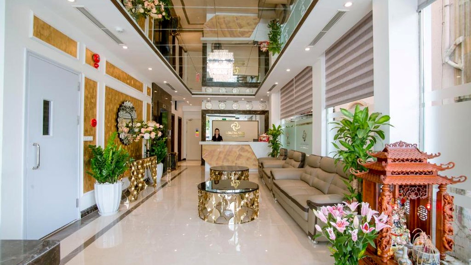 Khu chờ khách sạn dùng sofa, cây xanh và các bề mặt sáng để tăng cảm giác rộng rãi.