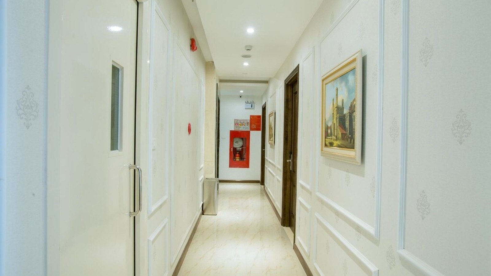 Hành lang khách sạn sáng, gọn với phào tường nhẹ và cửa gỗ tạo nhịp thị giác.