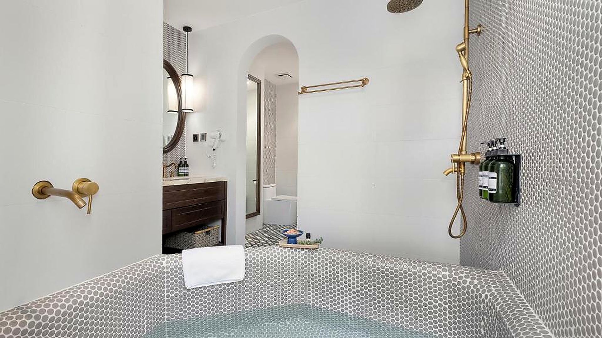 Phòng tắm khách sạn 4 sao hiện đại với gạch mosaic và thiết bị màu đồng.