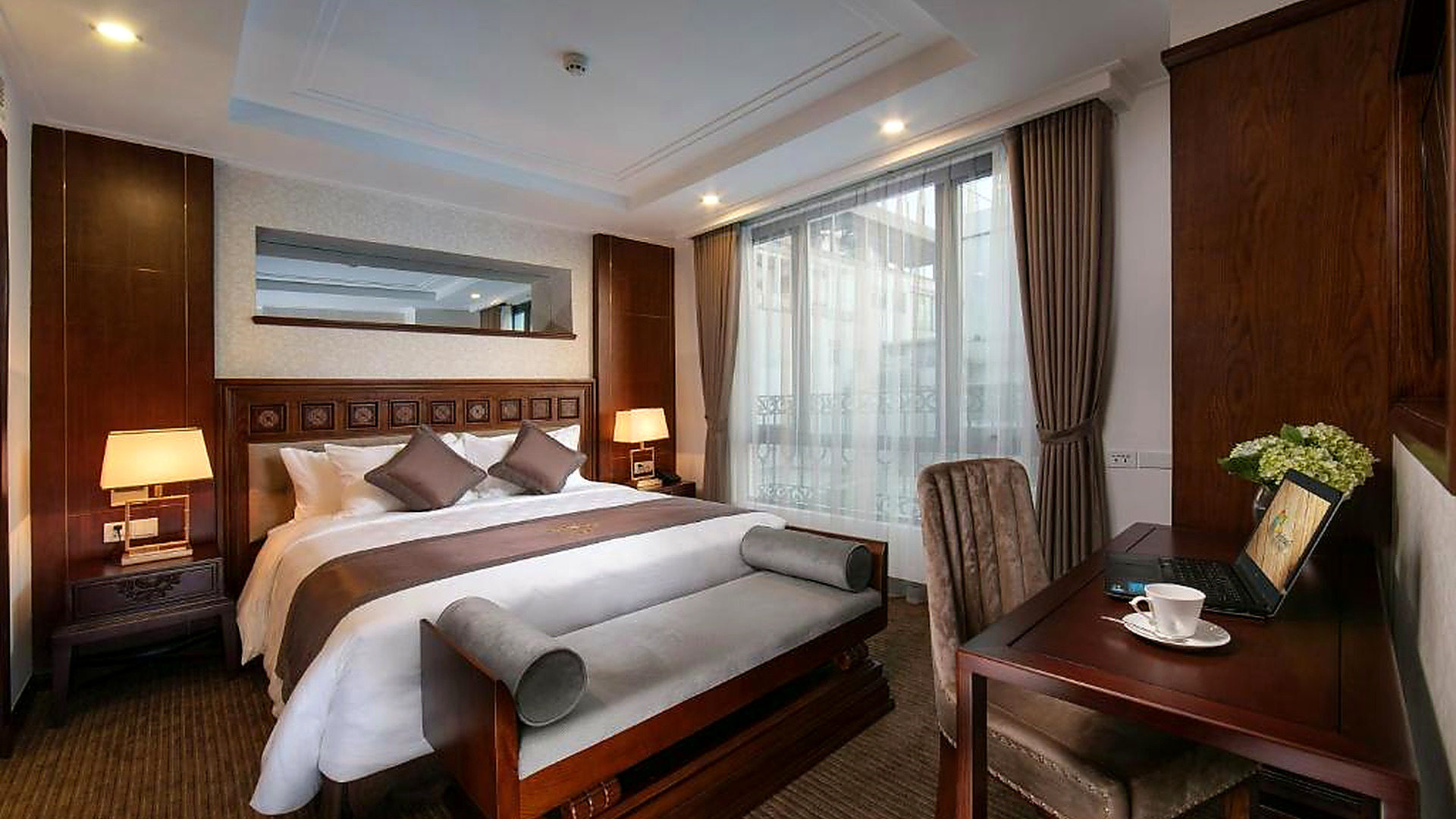 Phòng Deluxe sử dụng gỗ tối màu, vải bọc trung tính và hệ cửa kính lớn tạo cảm giác sang trọng, yên tĩnh.