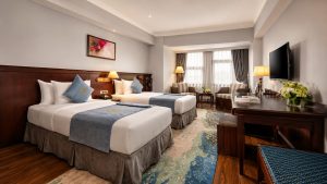 Phòng twin khách sạn 4 sao phong cách tân cổ điển với hai giường đơn, nội thất gỗ và ánh sáng ấm.