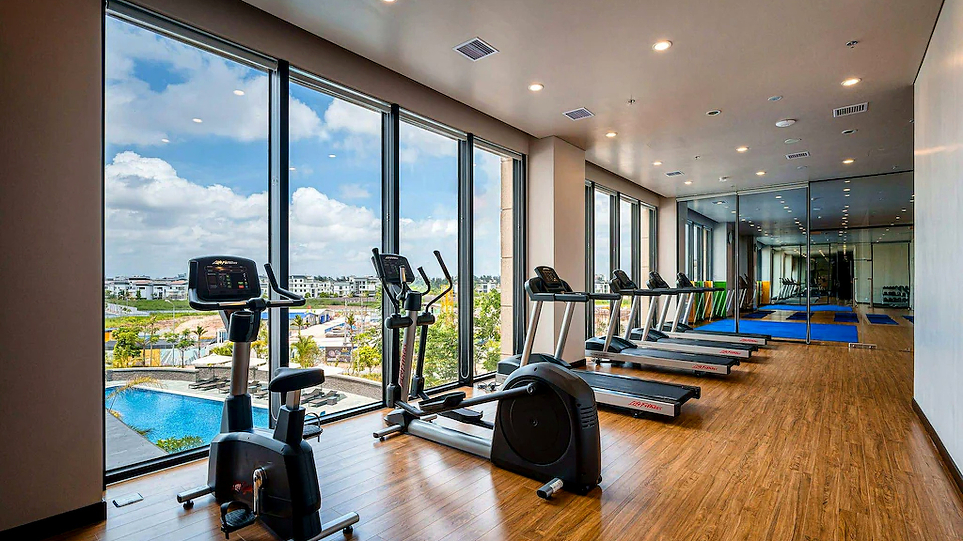Phòng gym sử dụng cửa kính lớn, thiết bị cardio và tầm nhìn thoáng.