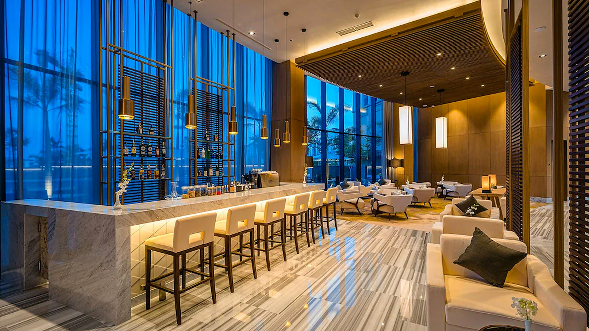 Quầy bar với mặt đá, ghế cao và cửa kính lớn phù hợp cho gặp gỡ và thư giãn buổi tối.