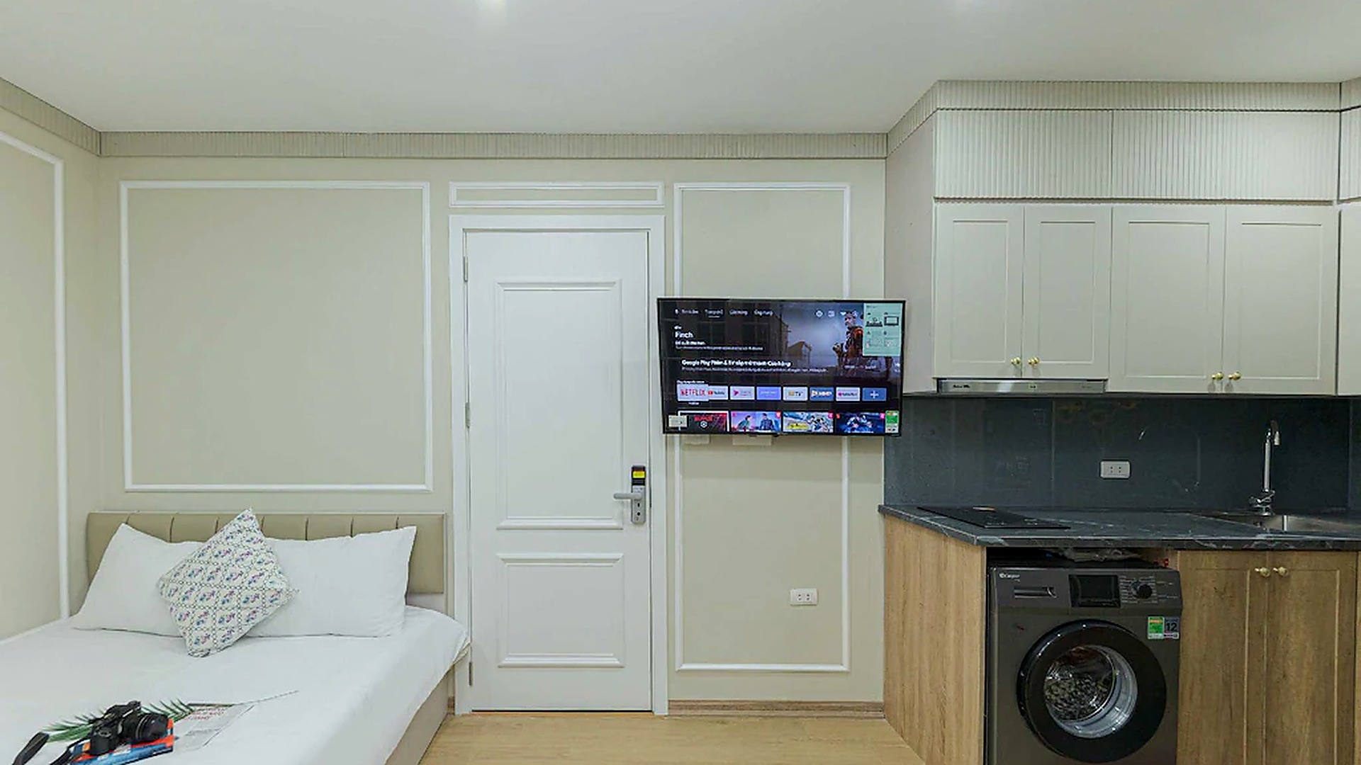 Phòng khách sạn 3 sao sáng thoáng với cửa sổ lớn, nội thất trắng kem và khu bếp nhỏ gọn.