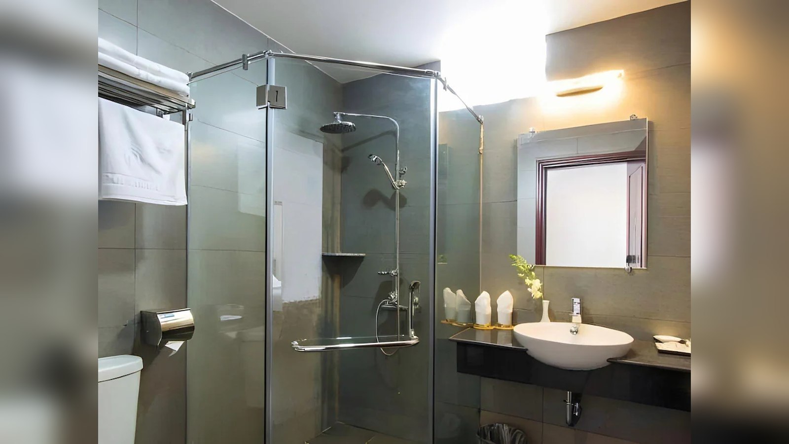 Phòng tắm khách sạn 2 sao sử dụng vách kính, tông xám và lavabo treo gọn gàng.