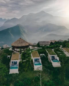 Những villa mái xanh và hồ bơi riêng được đặt theo cao độ, phía sau là các lớp núi chìm trong mây sớm.
