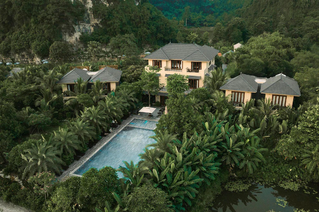 Những khối villa mái ngói xám được chia nhỏ và ẩn trong tán cây quanh hồ bơi trung tâm.