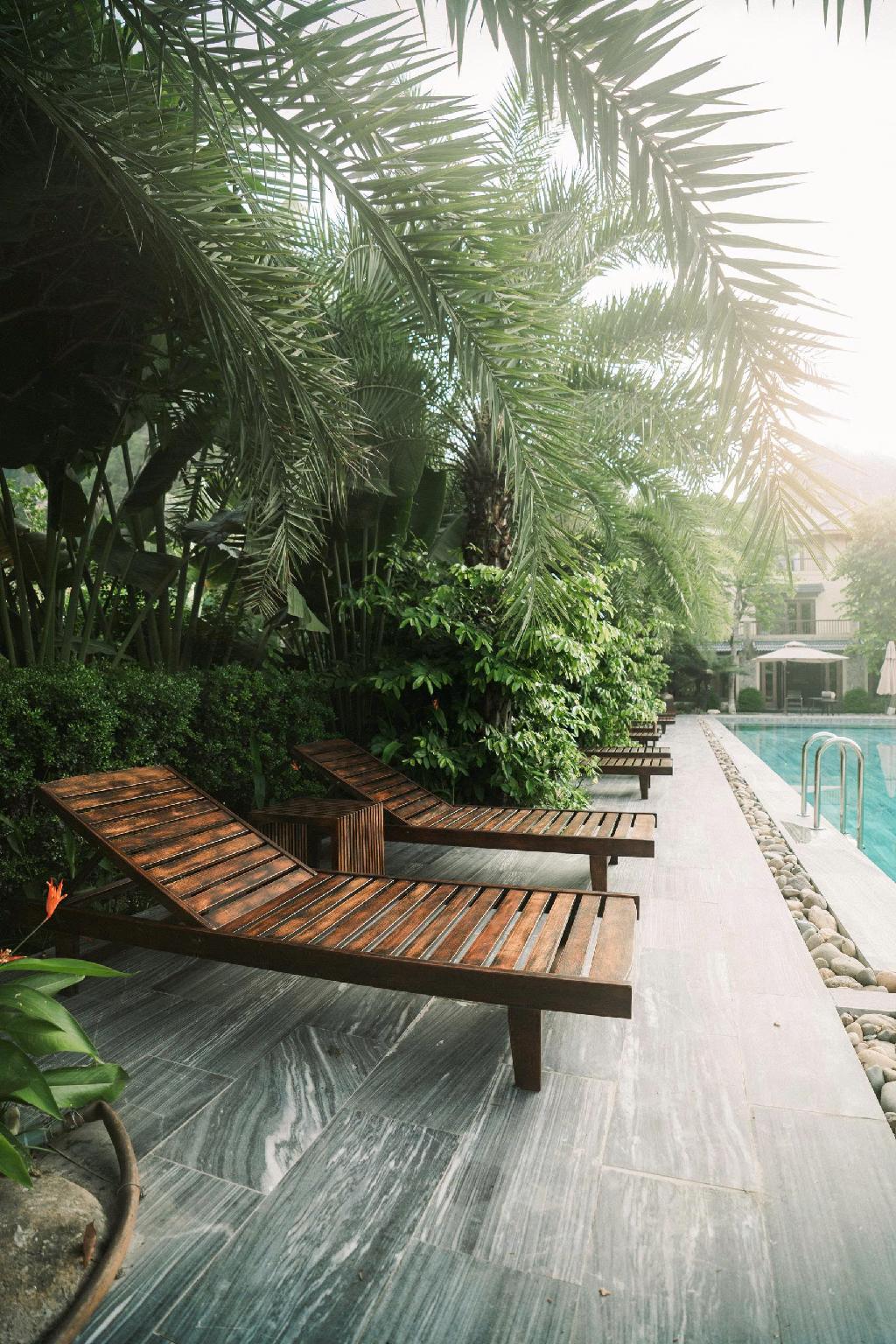 Giường gỗ lớn, đầu giường thêu, sàn đá và quạt trần hình lá tạo bản sắc Đông Dương nhiệt đới.