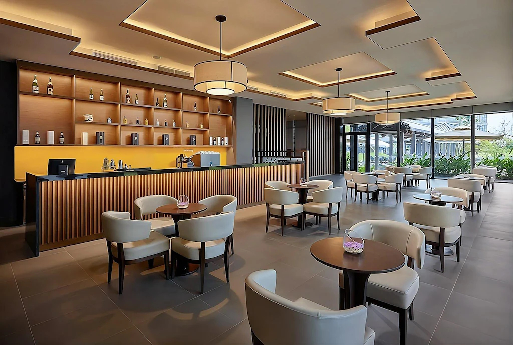 Quầy gỗ dài, trần có nhịp và ghế bọc sáng tạo một lounge hiện đại nhưng ấm.