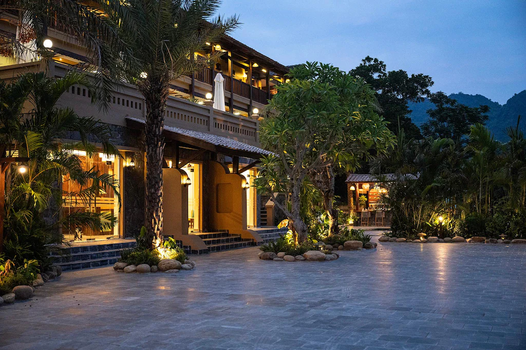 Lối vào lát đá cùng hàng cọ và ánh sáng thấp tạo cảm giác gần gũi.
