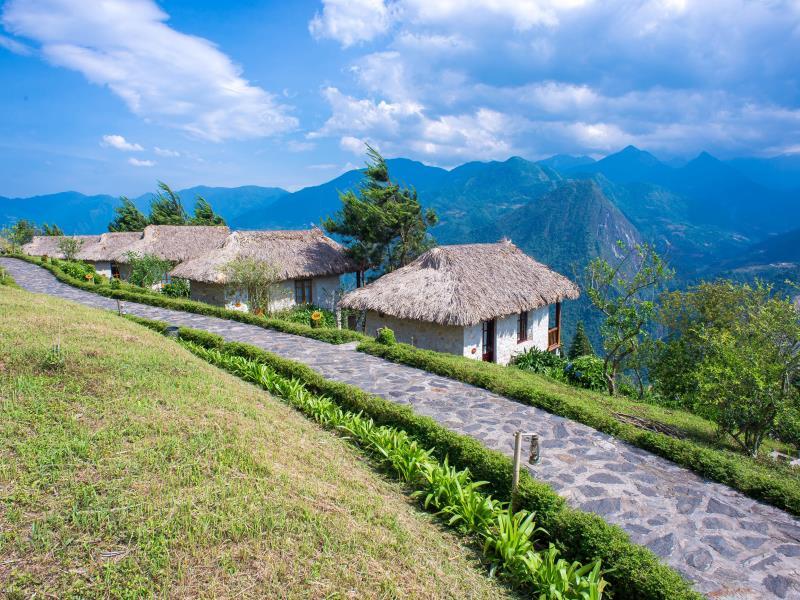 Đường dạo bám dốc, hàng cây thấp và mái tranh tạo nhịp chuyển mềm giữa kiến trúc với dãy núi.