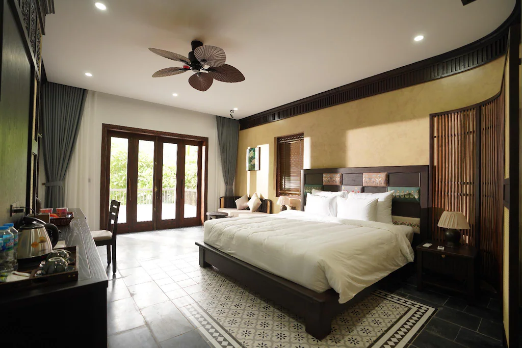 Giường gỗ lớn, đầu giường thêu, sàn đá và quạt trần hình lá tạo bản sắc Đông Dương nhiệt đới.