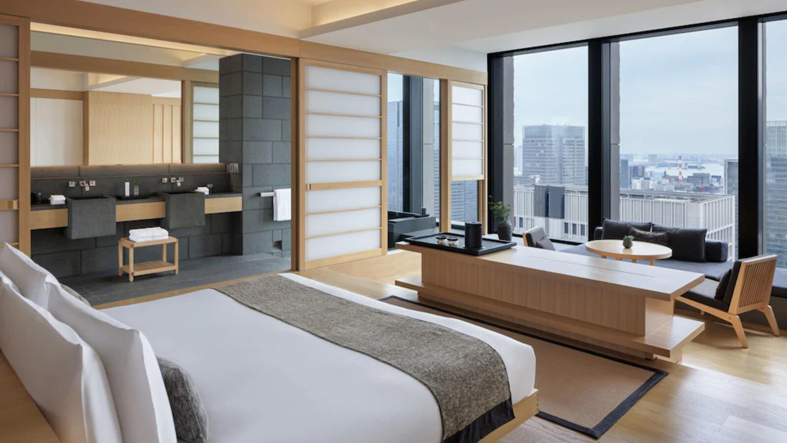 Phòng suite tổ chức theo lớp không gian mở, dùng gỗ sáng, vải thô và những đường nét tiết chế.