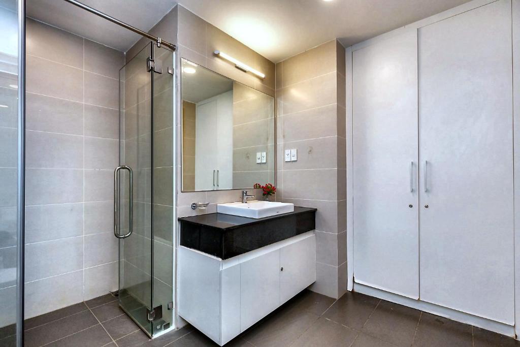 Phòng tắm dùng gạch trung tính, vách kính và tủ lavabo gọn để ưu tiên vệ sinh và sự tiện dụng.