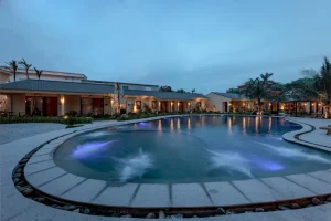 Hồ bơi uốn cong kết nối kiến trúc thấp tầng, hiên phòng và cảnh quan nhiệt đới.