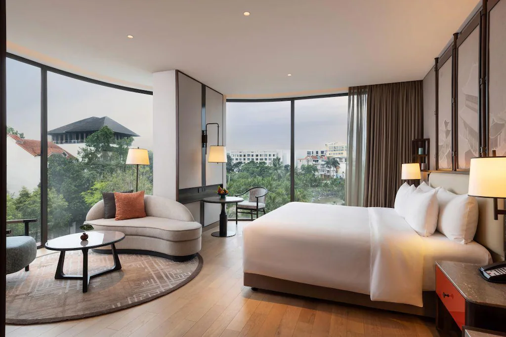 Cửa kính ôm góc đưa ánh sáng vào phòng ngủ, sofa cong tạo vùng thư giãn riêng.