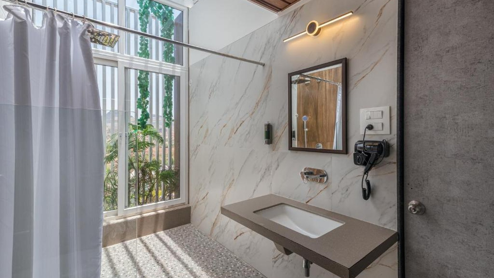 Suite mở liên kết giường, lounge và ban công qua các lớp kính và vật liệu màu khoáng.