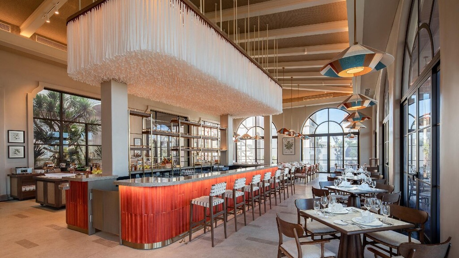 Quầy bar đỏ đất trở thành điểm nhấn dưới mái cao và chuỗi cửa vòm nhìn cảnh quan.