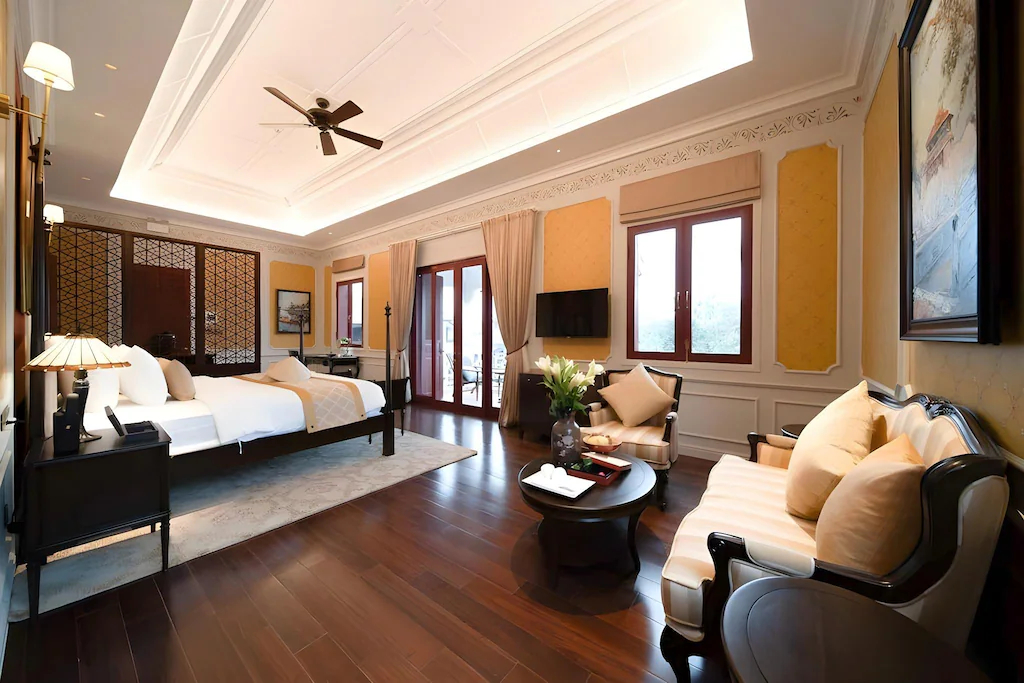 Phòng ngủ rộng tích hợp sofa và bàn trà, dùng vàng đất, xanh lam cùng gỗ tối để phân vùng mà không cần vách kín.