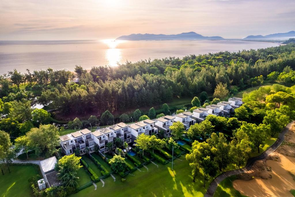 Dãy villa thấp tầng nằm giữa thảm cỏ và rừng ven biển, đón ánh sáng sớm từ mặt nước.