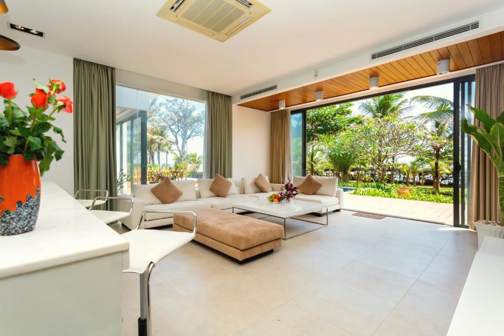 Phòng sinh hoạt dùng sofa sáng, trần gỗ và hệ cửa mở toàn phần để nối nội thất với sân vườn.