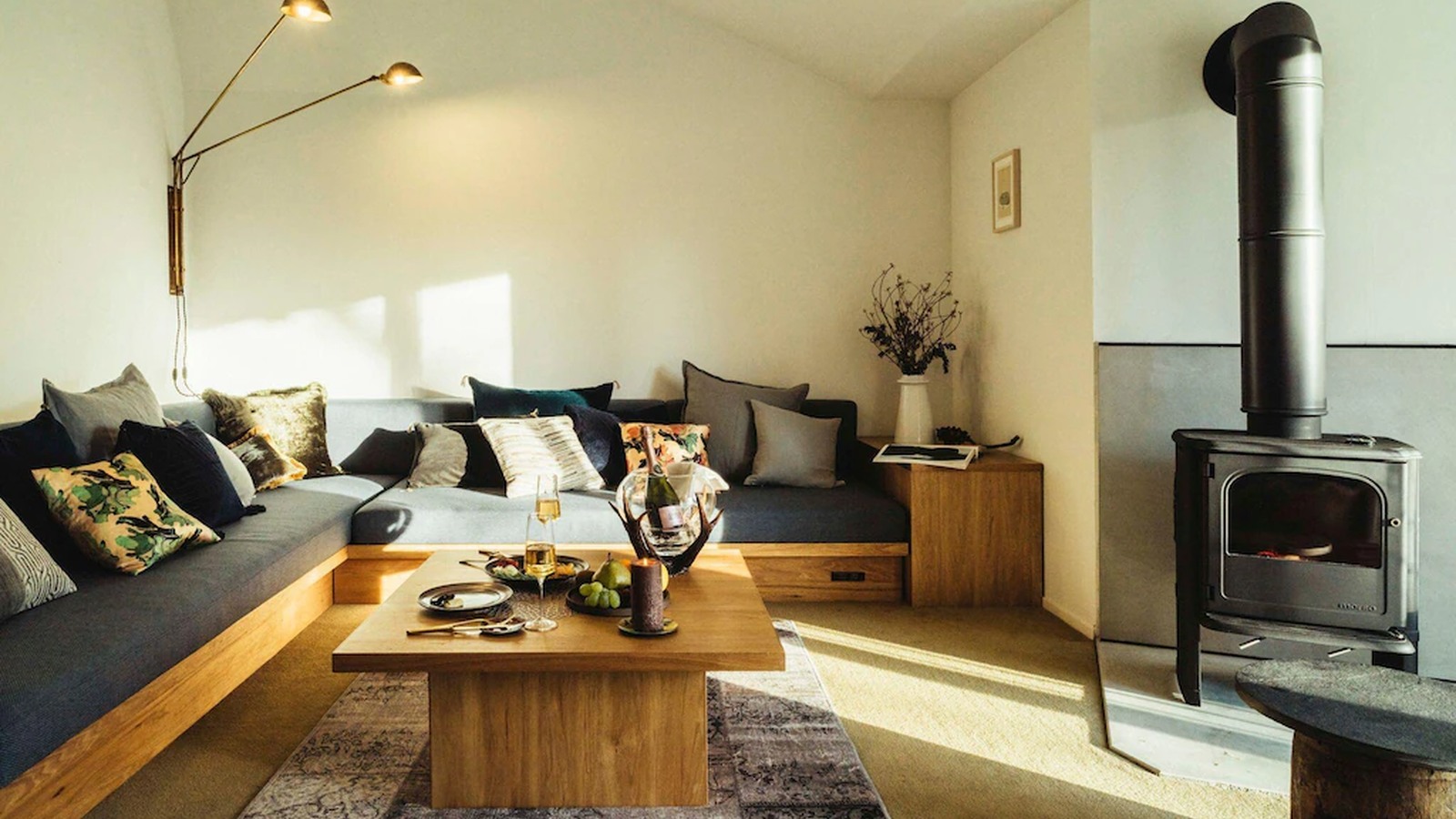 Lò sưởi đen, sofa dài và bàn gỗ nguyên khối tạo một phòng khách ấm áp, giàu xúc giác.