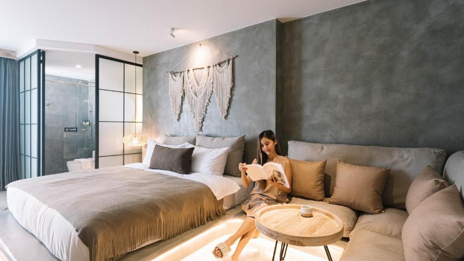 Phòng giường đôi kết hợp sofa dài, bàn trà thấp và đồ dệt thủ công, tạo một vùng nghỉ đủ thoải mái mà không cần trang trí cầu kỳ.