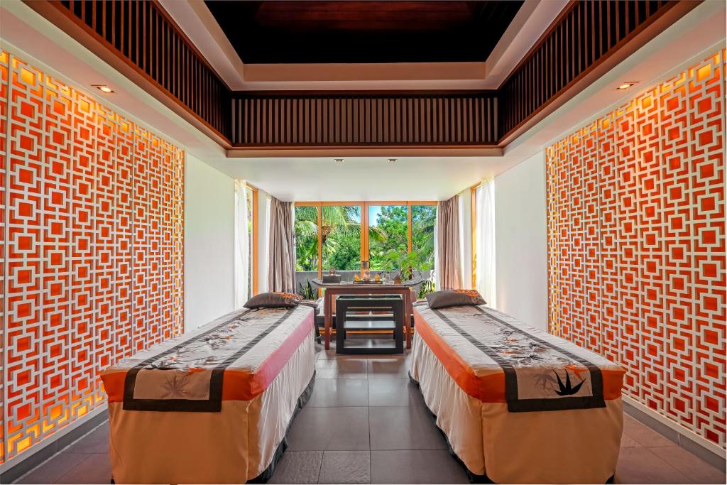 Phòng trị liệu đôi sử dụng trần gỗ tối, vách hoa văn phát sáng và bảng màu cam đất để tạo cảm giác ấm.