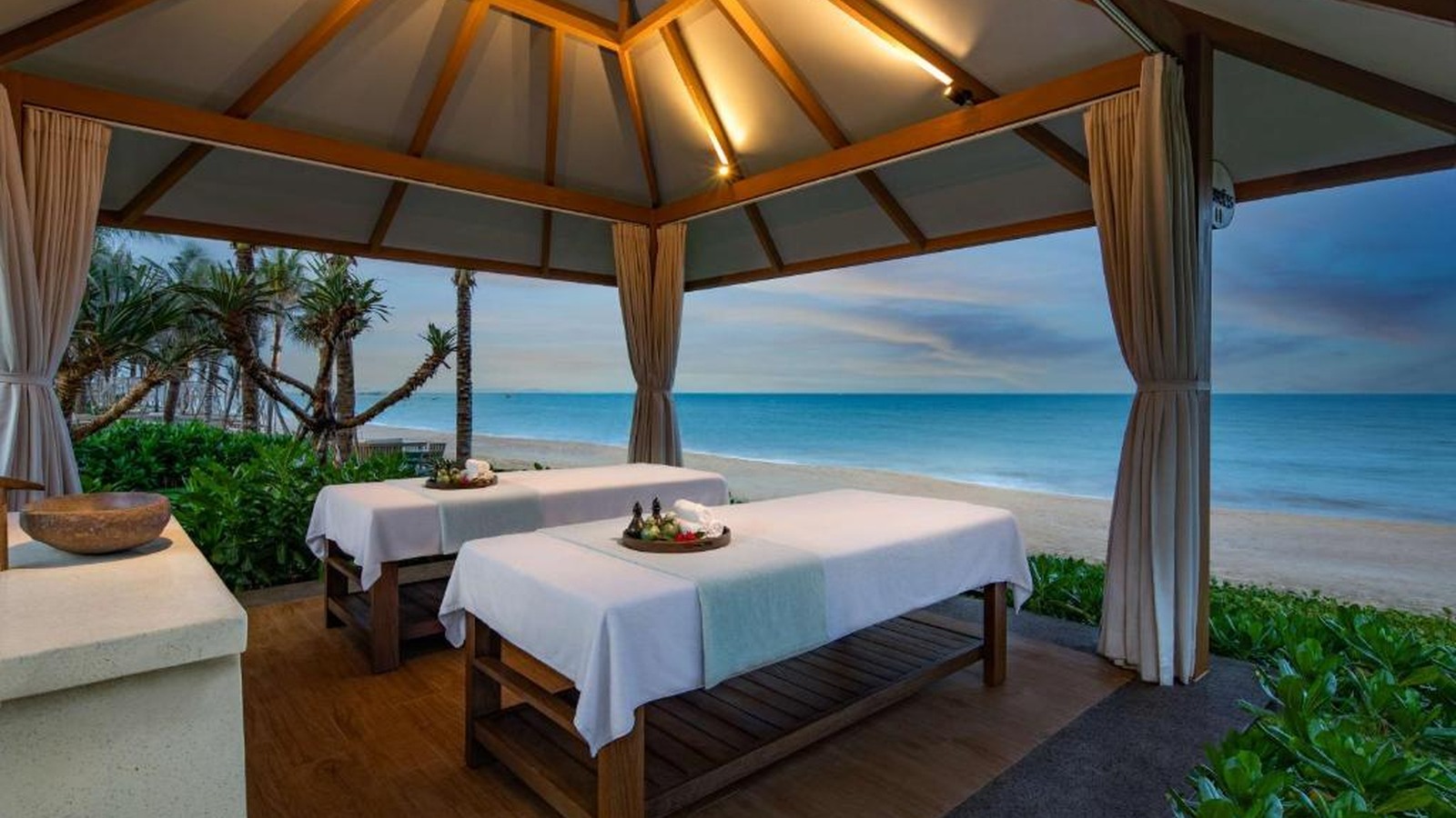 Pavilion trị liệu riêng tư mở ra biển, kết hợp rèm mềm, mái dốc và vườn thấp.