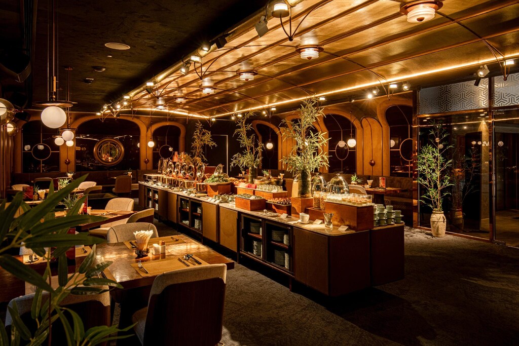 Khu buffet khách sạn 4 sao với quầy trung tâm, đèn trần ánh đồng và cây trang trí