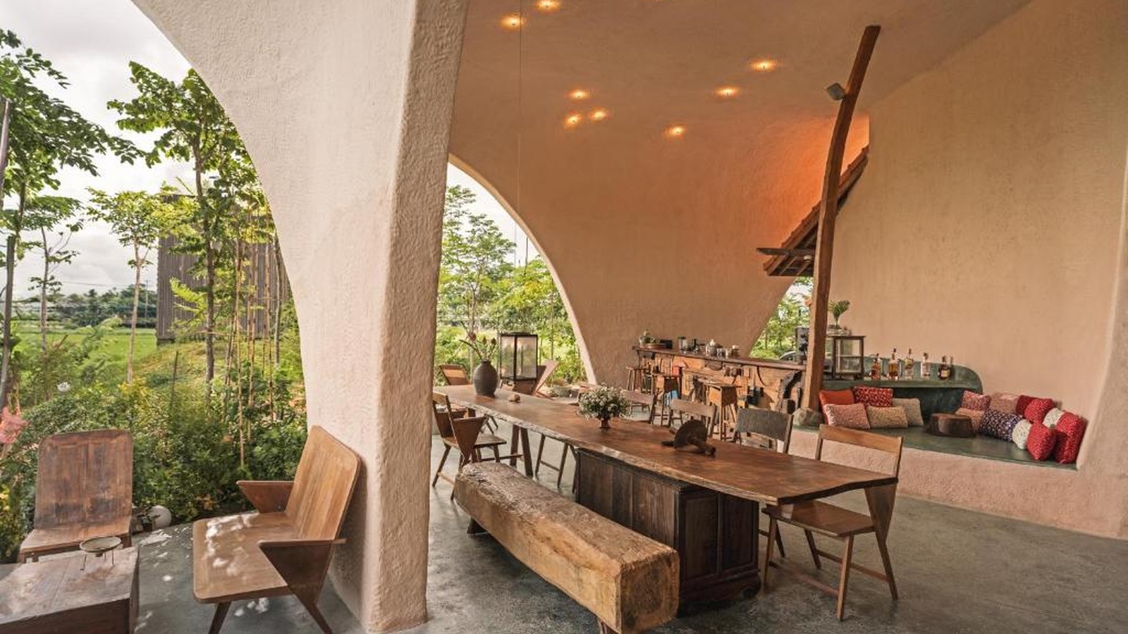 Quầy bar và lounge nằm dưới mái vòm lớn, kết hợp gỗ có dấu thời gian với khu vườn nhiệt đới ở ngay mép ngồi.