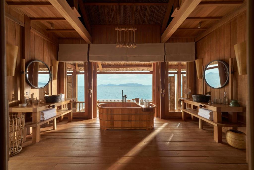 Bồn ngâm đặt trên trục nhìn, hai lavabo đối xứng và ánh sáng tự nhiên tạo cảm giác spa riêng trong phòng.
