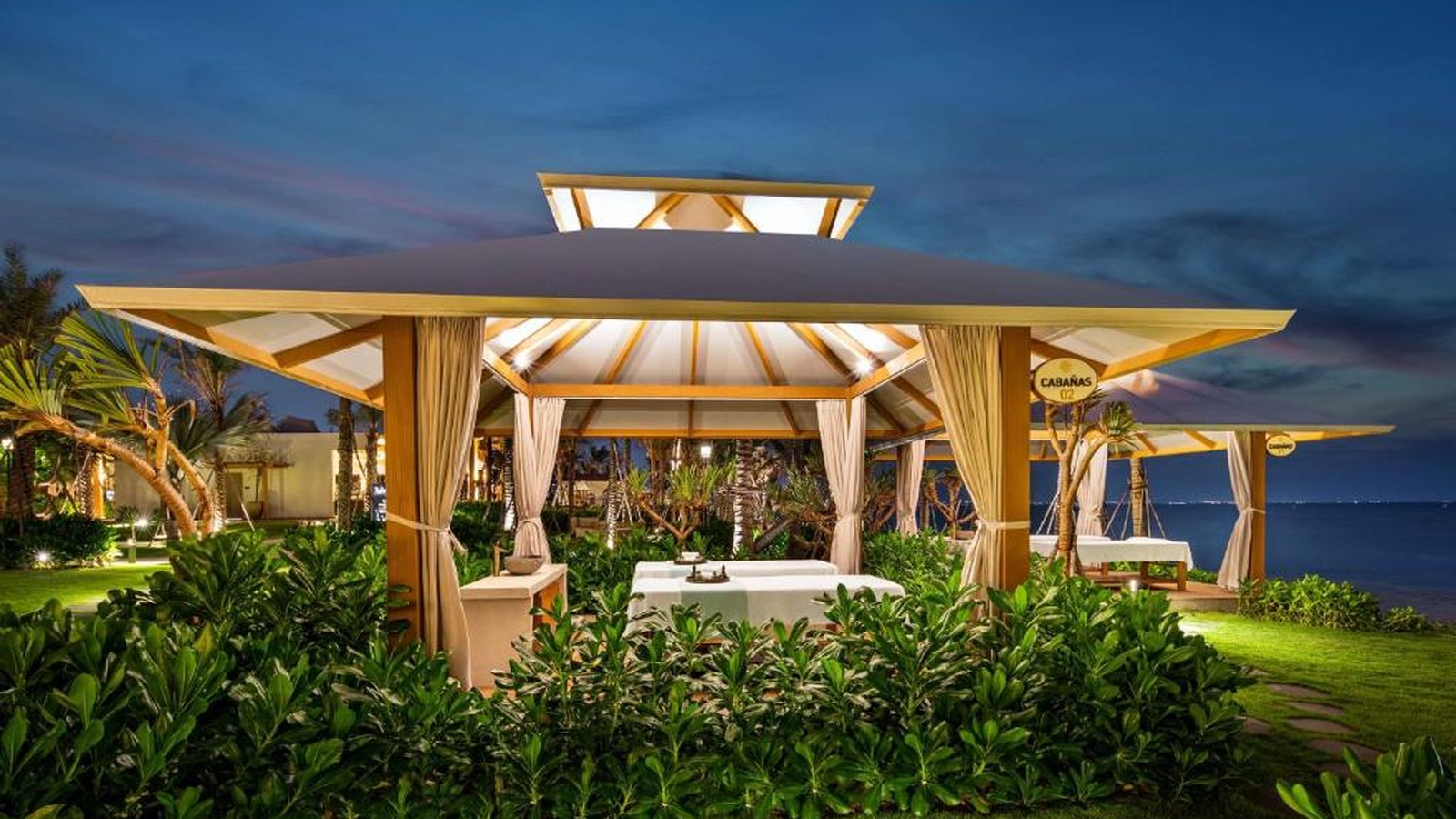 Pavilion mái xòe phát sáng giữa vườn như một điểm dừng cho nghi thức và sự kiện nhỏ.
