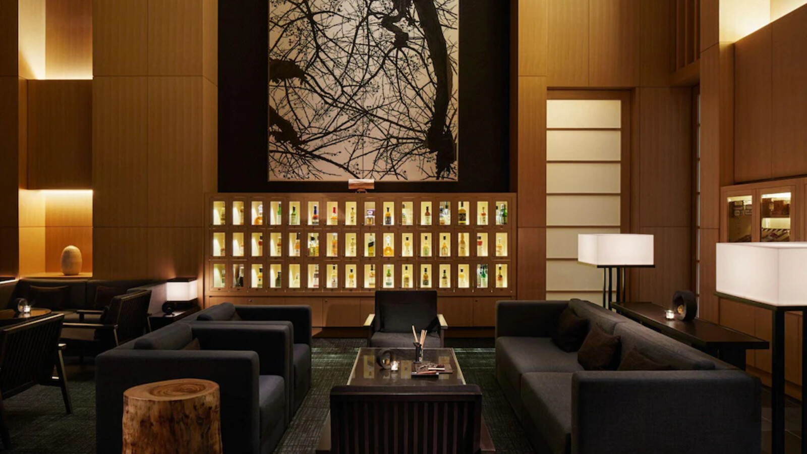 Bar lounge khai thác gỗ tối, vải xám, ánh sáng hắt và một tác phẩm đơn sắc làm điểm neo thị giác.