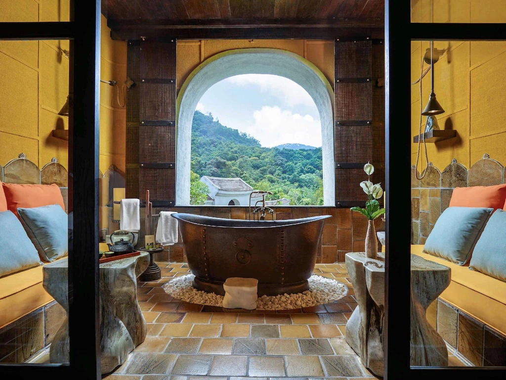 Bồn tắm độc lập trở thành tâm điểm giữa gạch đất nung, gỗ sẫm và cảnh quan.