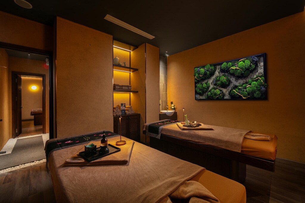 Phòng spa đôi khách sạn Indochine với hai giường trị liệu, ánh sáng vàng và tranh rêu xanh