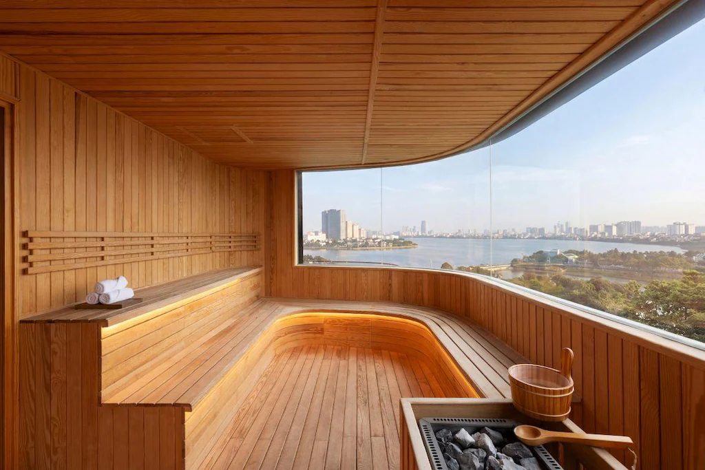 Không gian sauna ốp gỗ toàn bộ, ghế cong và cửa kính rộng hướng ra cảnh quan.