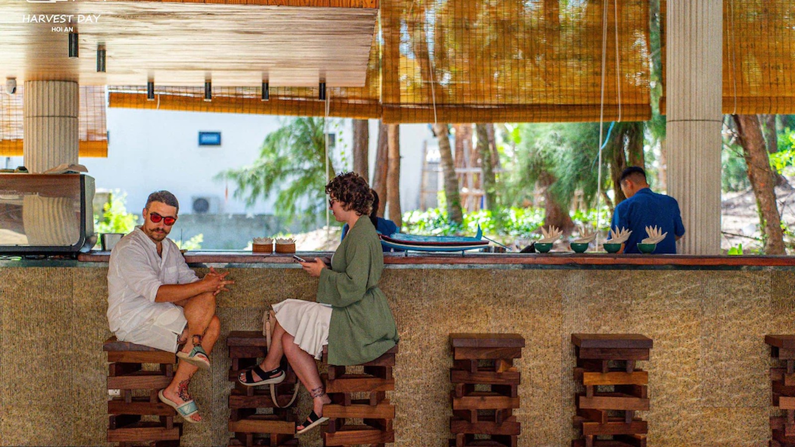 Quầy bar mở dùng gỗ thô, ghế ghép mộc và mành tre để giữ bầu không khí thân mật.