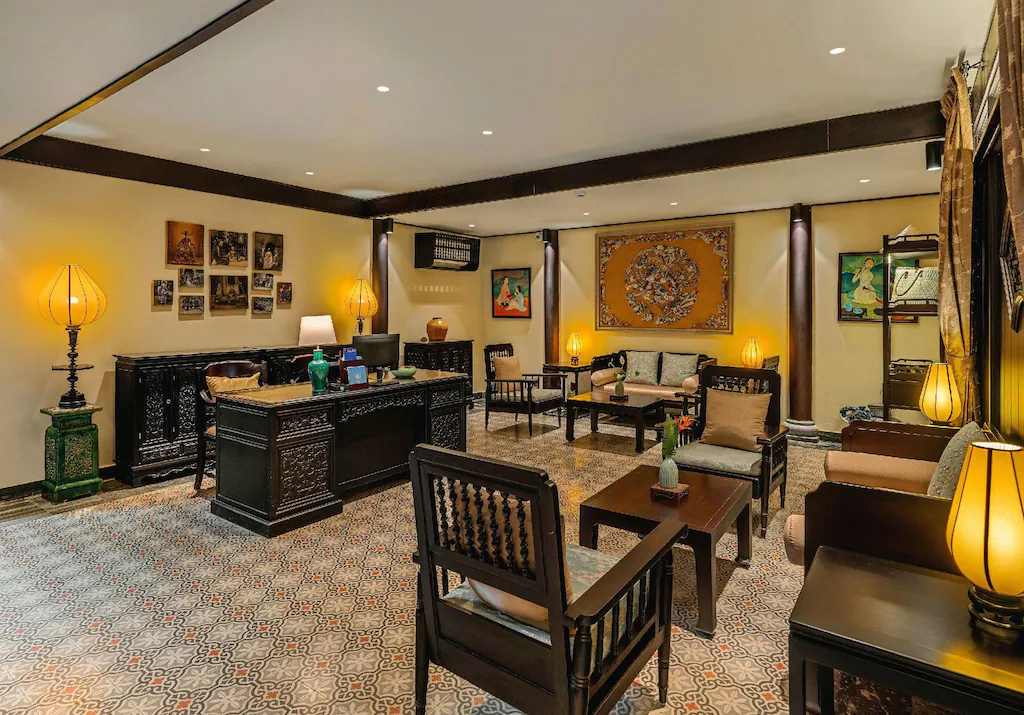 Quầy gỗ, ghế bọc, đèn vàng và tranh sắp đặt tạo một lounge mang sắc thái thư viện và phòng khách lớn.