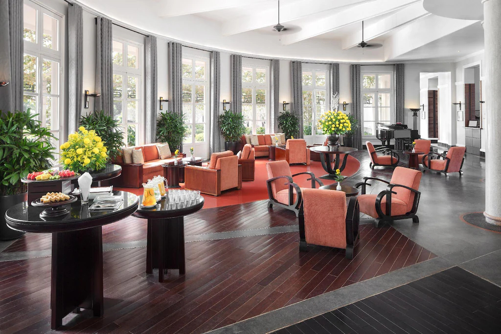 Cửa cao đưa ánh sáng vào lounge, cân bằng đồ gỗ tối, ghế sáng và các cụm cây.