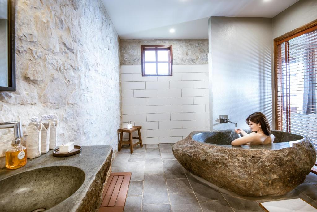 Bồn đá điêu khắc trở thành tâm điểm wellness, kết hợp sàn đá nhám và ô cửa lấy sáng kín đáo.