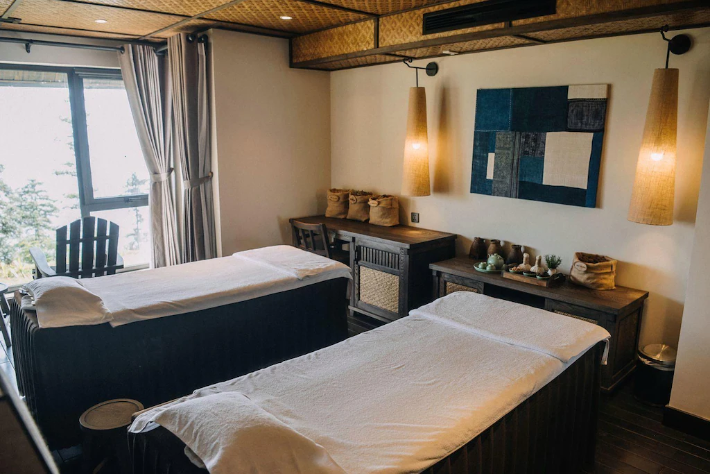 Hai giường trị liệu, vải dệt và gỗ tối tạo một không gian spa riêng tư, yên tĩnh và giàu cảm giác xúc giác.