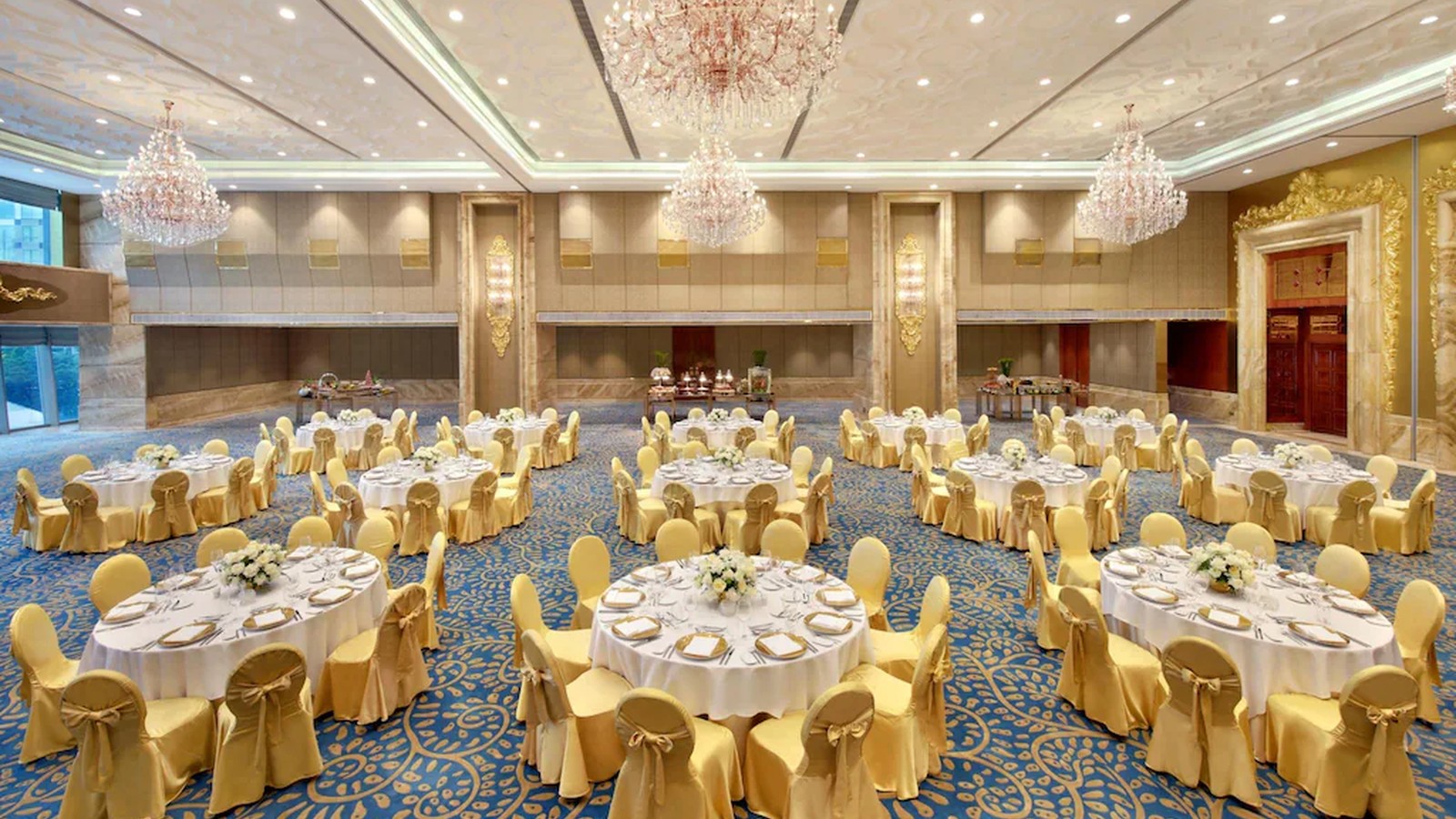 Ballroom bố trí bàn tròn, ghế vàng và đèn chùm pha lê cho không gian tiệc trang trọng