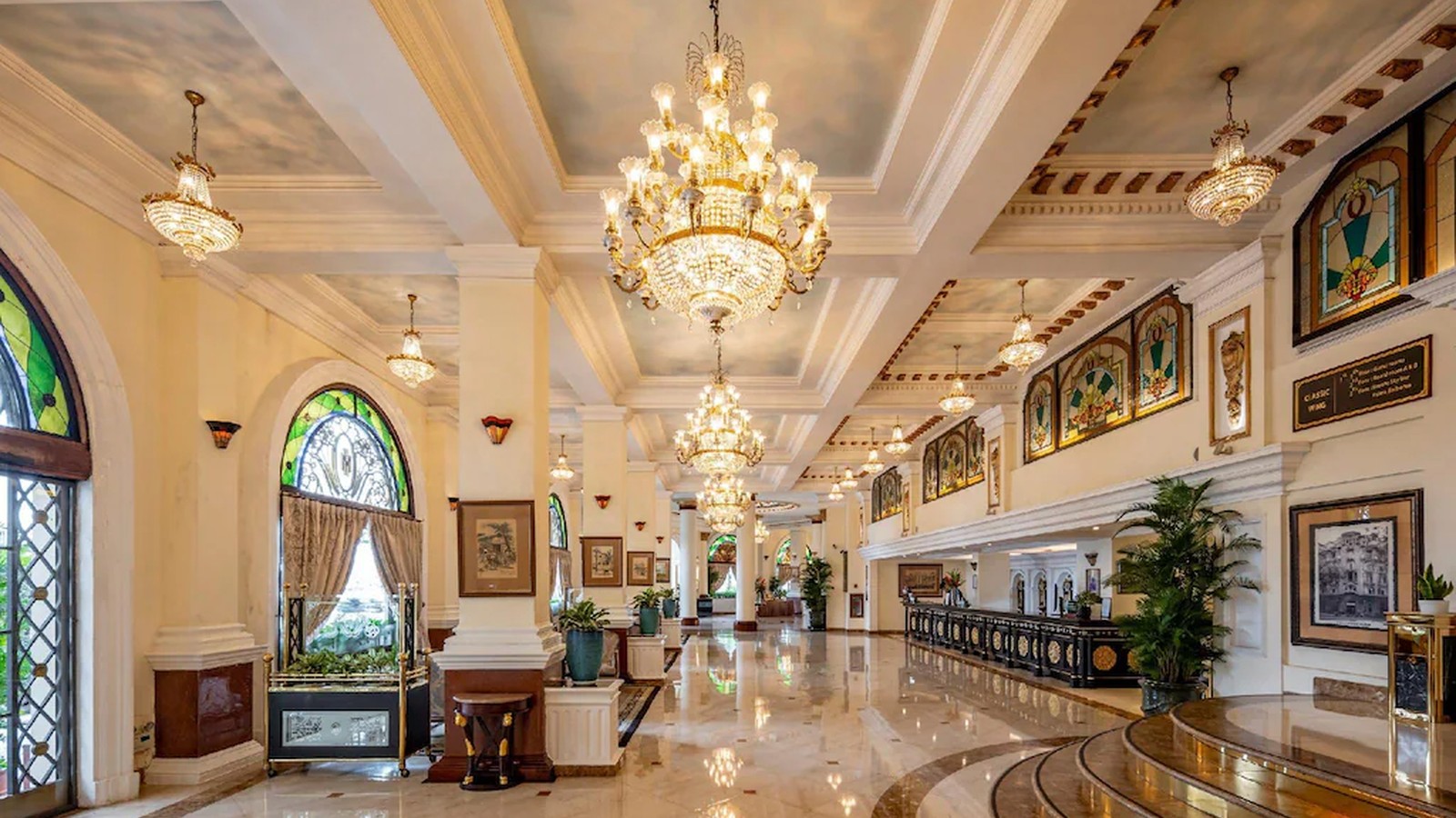 Đại sảnh Indochine nhấn mạnh nhịp cột, cửa vòm kính màu và ánh sáng phản chiếu trên nền đá.