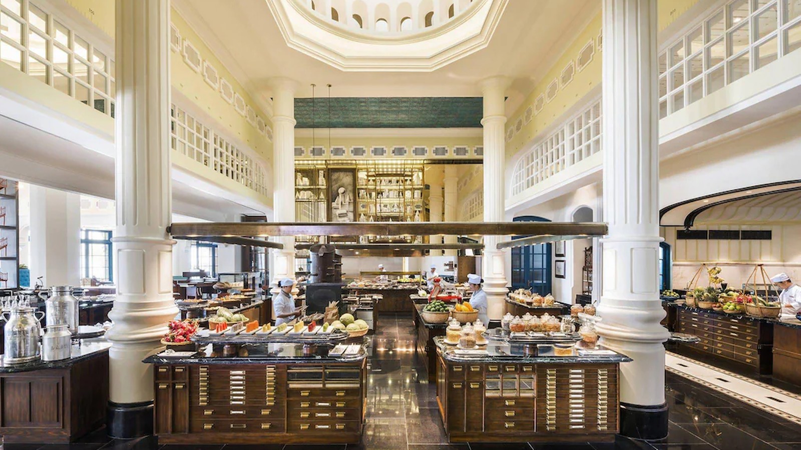 Nhà hàng buffet dùng trần cao, cột trắng và quầy đảo để tạo luồng phục vụ rõ ràng.