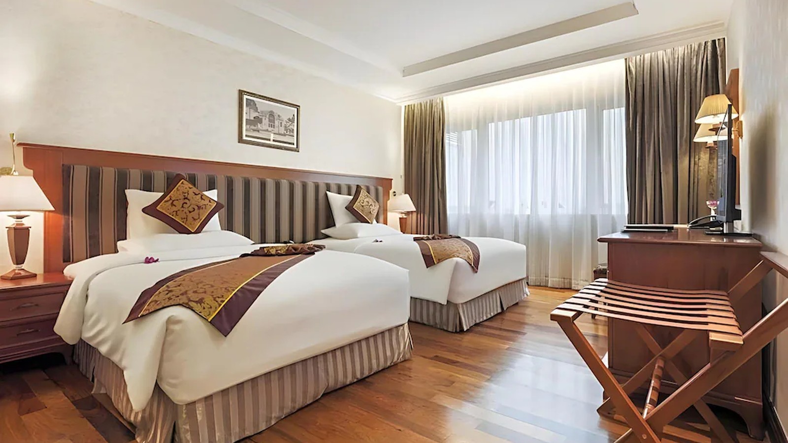 Phòng hai giường Indochine cân bằng sàn gỗ, nội thất nâu và ánh sáng tự nhiên.