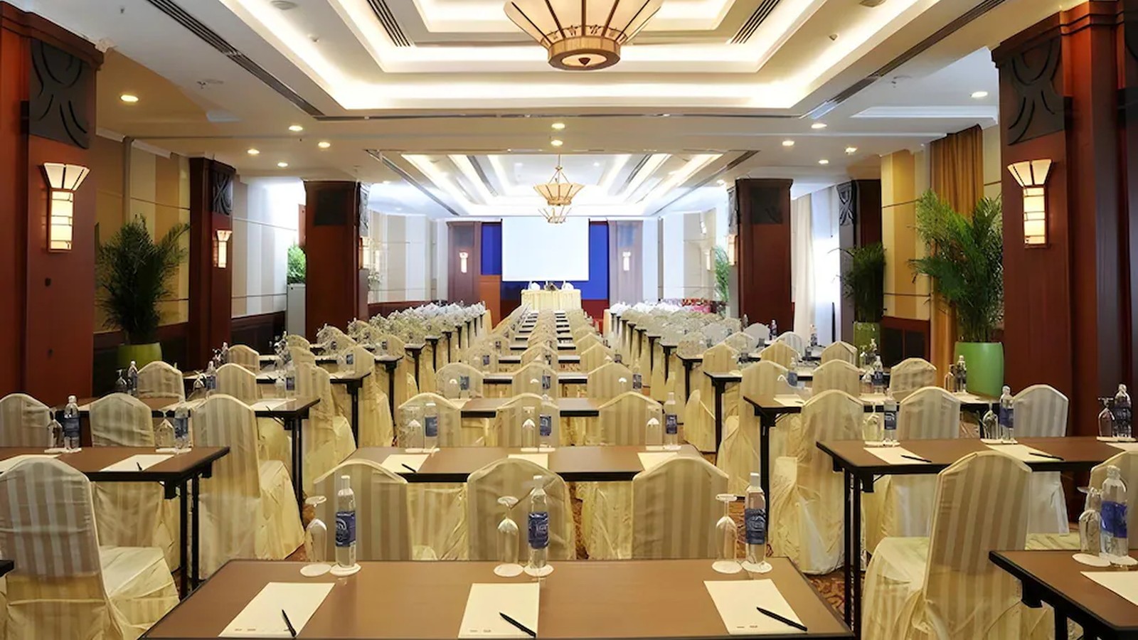 Phòng hội nghị bố trí lớp học, màn chiếu lớn và lối đi rõ cho chương trình doanh nghiệp.