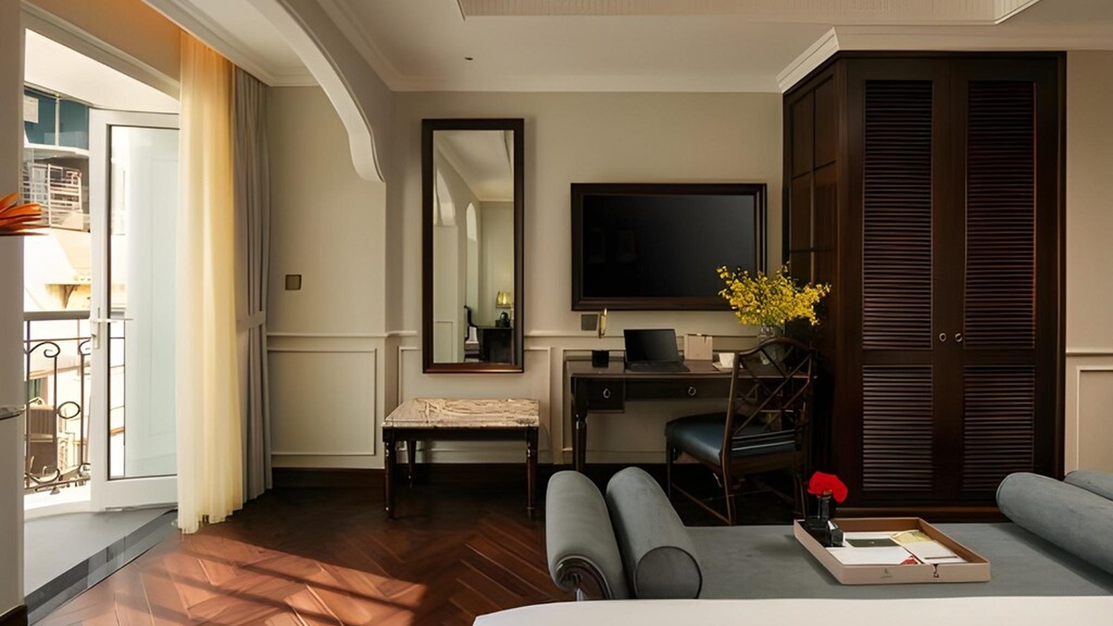 Suite có ban công kết hợp bàn làm việc gỗ, tủ cửa chớp và sàn xương cá trong bố cục thoáng.